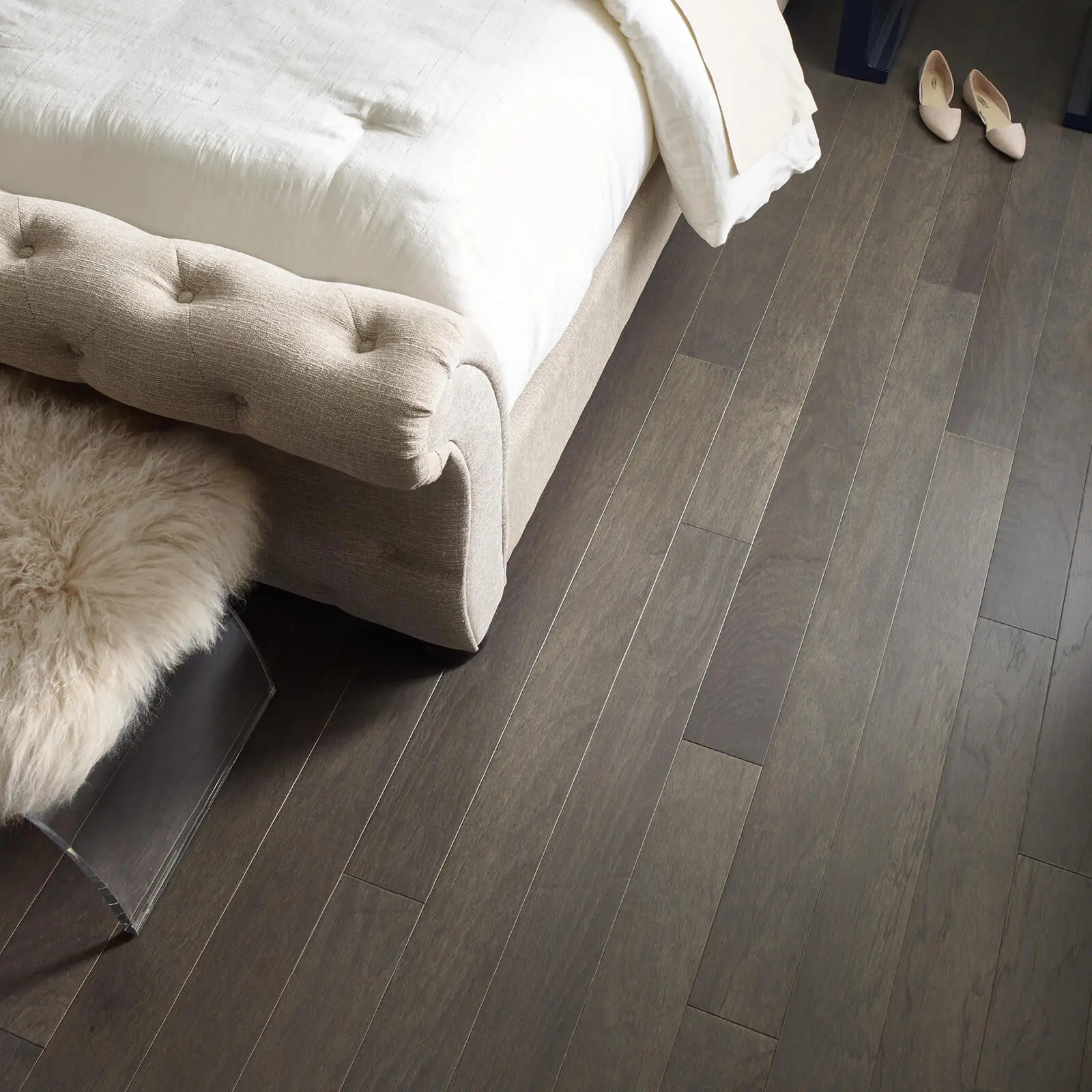 Dark-stained hardwood flooring planks installed in a bedroom next to a beige bench.