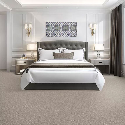 Symmetrical bedroom featuring plush beige carpeting, a tufted gray headboard with white linens, and matching gray nightstands against a paneled wall.