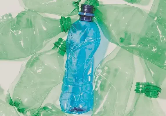 A top-down view of crumpled, empty plastic bottles, highlighting one blue bottle centered among several green ones.
