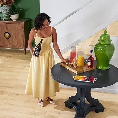 Woman in a yellow dress setting up drinks over light wood flooring.