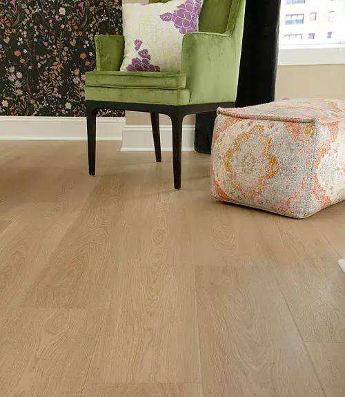 Light natural wood-look flooring next to a green armchair and patterned ottoman.