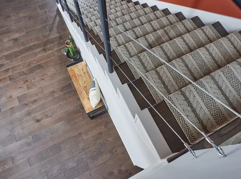 Geometric patterned carpet runner on a dark wood staircase.