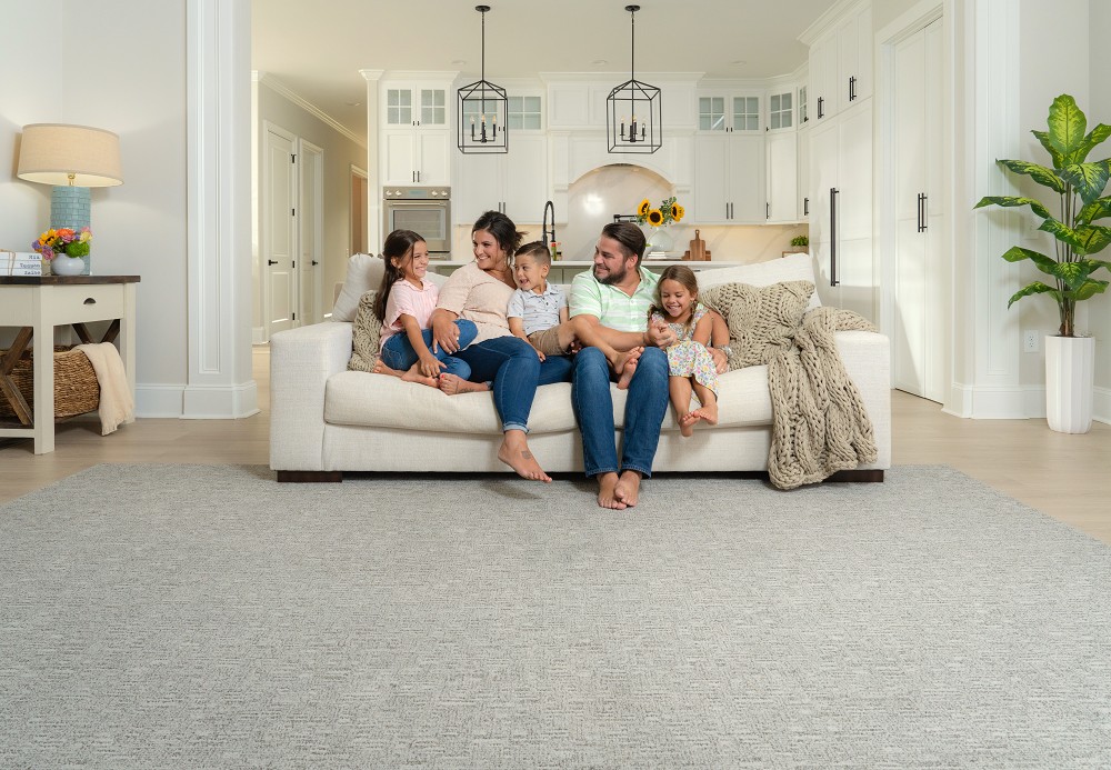 Family sitting together on a couch over light gray patterned carpet.