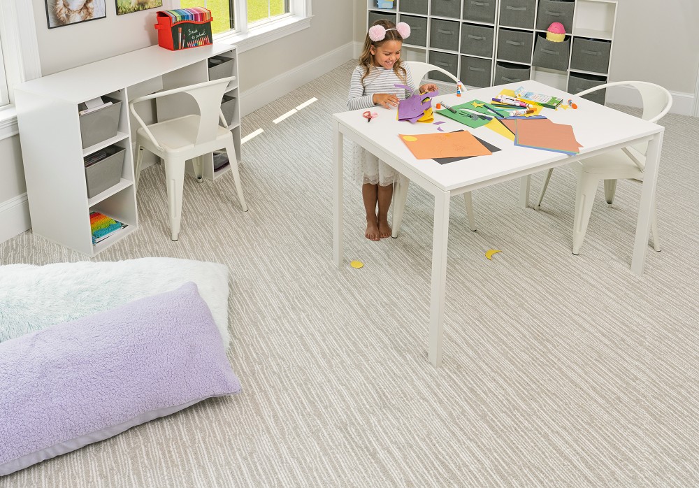 Playroom with light gray wavy-textured carpet and a child doing crafts.
